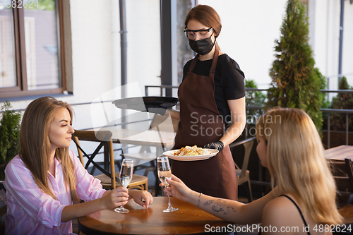 Image of The waitress works in a restaurant in a medical mask, gloves during coronavirus pandemic