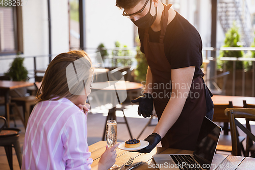 Image of The waiter works in a restaurant in a medical mask, gloves during coronavirus pandemic