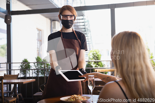 Image of The waitress works in a restaurant in a medical mask, gloves during coronavirus pandemic