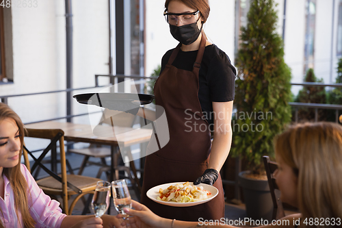 Image of The waitress works in a restaurant in a medical mask, gloves during coronavirus pandemic
