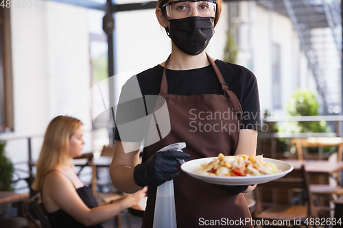 Image of The waitress works in a restaurant in a medical mask, gloves during coronavirus pandemic