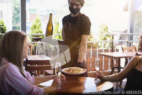 Image of The waitress works in a restaurant in a medical mask, gloves during coronavirus pandemic