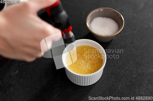 Image of hand with burner making sugar crust in baking dish