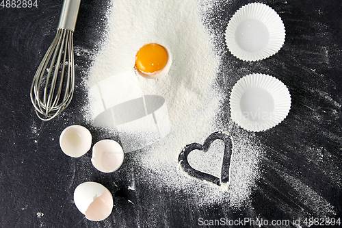 Image of flour, egg, whisk and paper baking molds on table