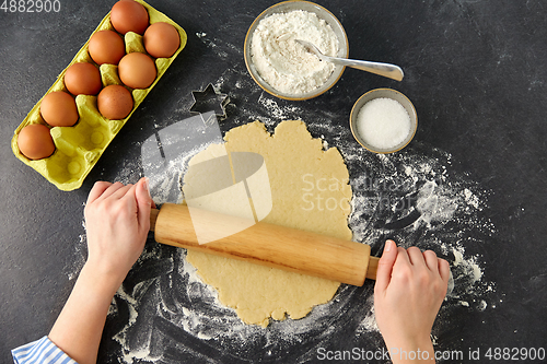 Image of hands with rolling pin rolling dough on table