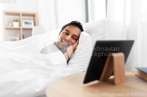 Image of indian man looking at tablet pc in bed at home