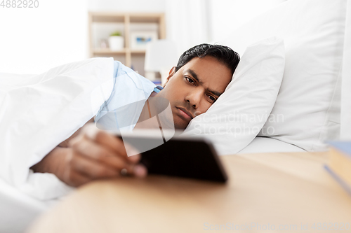 Image of sleepy indian man with smartphone lying in bed