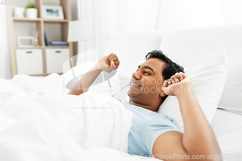 Image of happy indian man stretching in bed at home