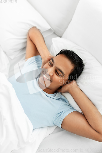 Image of happy indian man lying in bed at home