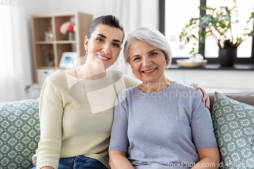 Image of senior mother with adult daughter hugging at home