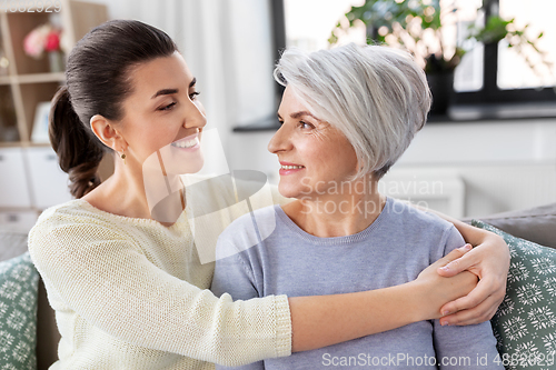 Image of senior mother with adult daughter hugging at home