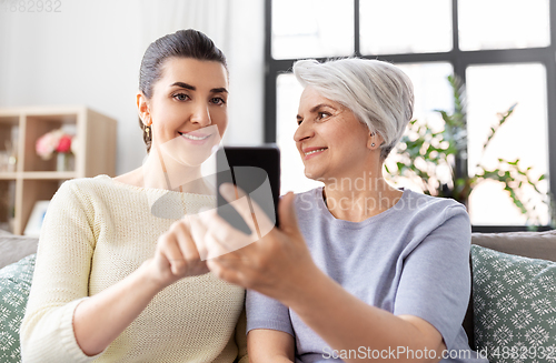 Image of daughter and senior mother with smartphone at home