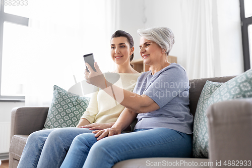 Image of senior mother with daughter taking selfie at home