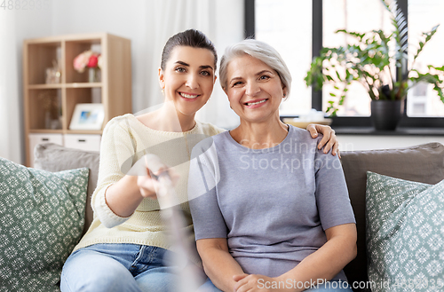 Image of senior mother with daughter taking selfie at home