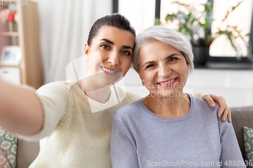 Image of senior mother with daughter taking selfie at home