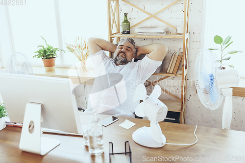 Image of Businessman, manager in office with computer and fan cooling off, feeling hot, flushed