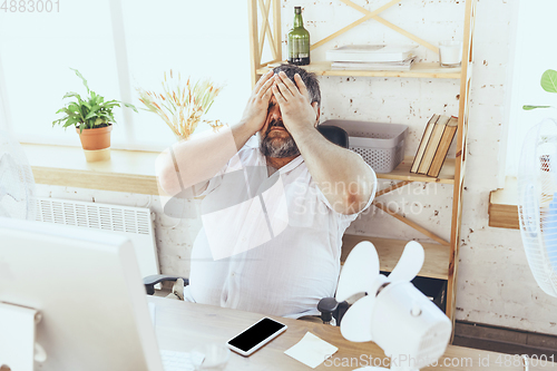 Image of Businessman, manager in office with computer and fan cooling off, feeling hot, flushed