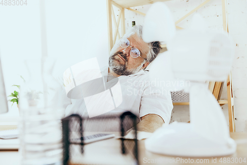 Image of Businessman, manager in office with computer and fan cooling off, feeling hot, flushed