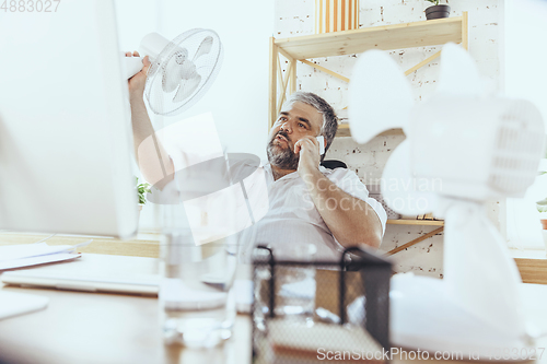 Image of Businessman, manager in office with computer and fan cooling off, feeling hot, flushed