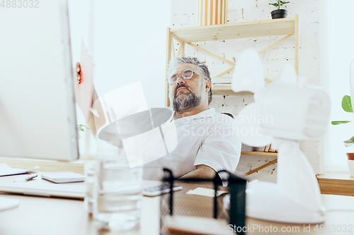 Image of Businessman, manager in office with computer and fan cooling off, feeling hot, flushed