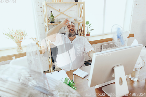 Image of Businessman, manager in office with computer and fan cooling off, feeling hot, flushed