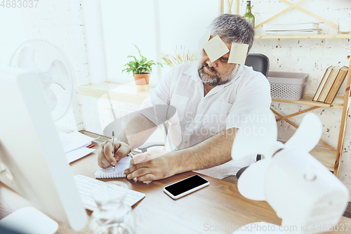 Image of Businessman, manager in office with computer and fan cooling off, feeling hot, flushed