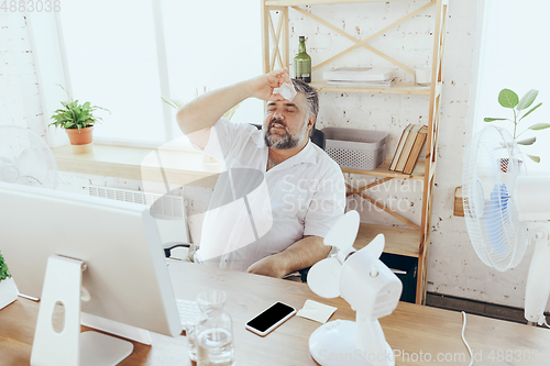 Image of Businessman, manager in office with computer and fan cooling off, feeling hot, flushed