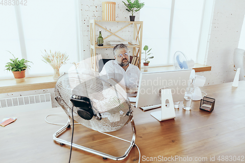 Image of Businessman, manager in office with computer and fan cooling off, feeling hot, flushed