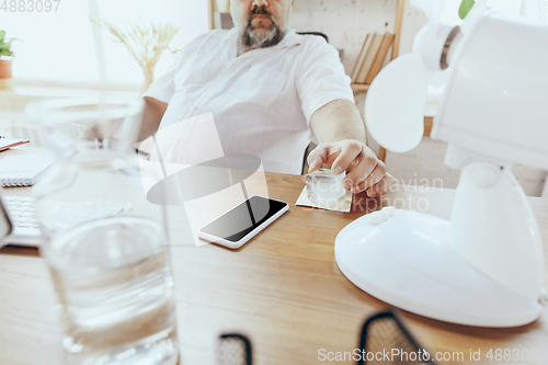 Image of Businessman, manager in office with computer and fan cooling off, feeling hot, flushed