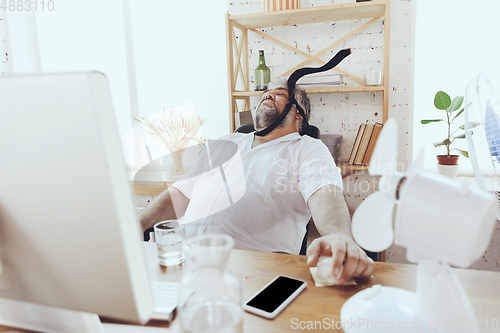 Image of Businessman, manager in office with computer and fan cooling off, feeling hot, flushed