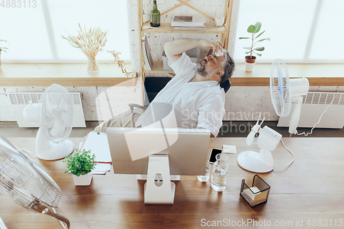 Image of Businessman, manager in office with computer and fan cooling off, feeling hot, flushed