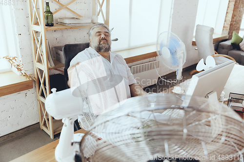 Image of Businessman, manager in office with computer and fan cooling off, feeling hot, flushed