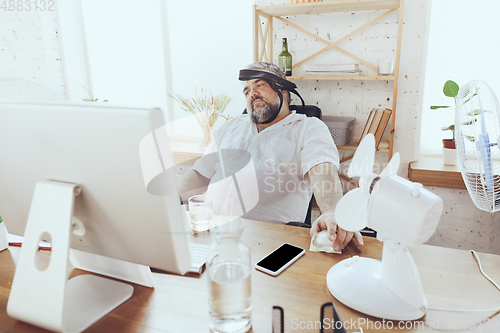 Image of Businessman, manager in office with computer and fan cooling off, feeling hot, flushed