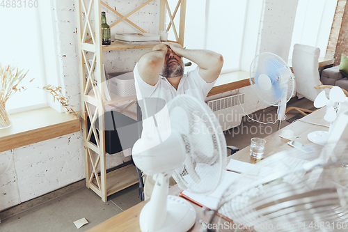 Image of Businessman, manager in office with computer and fan cooling off, feeling hot, flushed