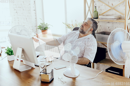 Image of Businessman, manager in office with computer and fan cooling off, feeling hot, flushed