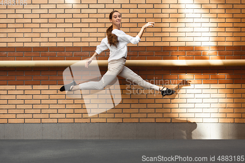 Image of Jumping young woman in front of buildings, on the run in jump high