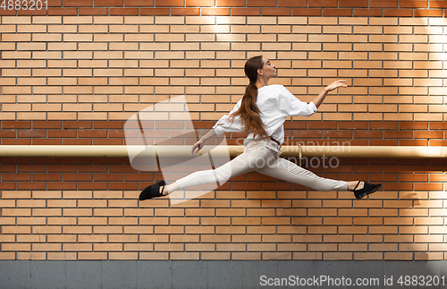 Image of Jumping young woman in front of buildings, on the run in jump high