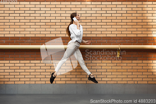 Image of Jumping young woman in front of buildings, on the run in jump high