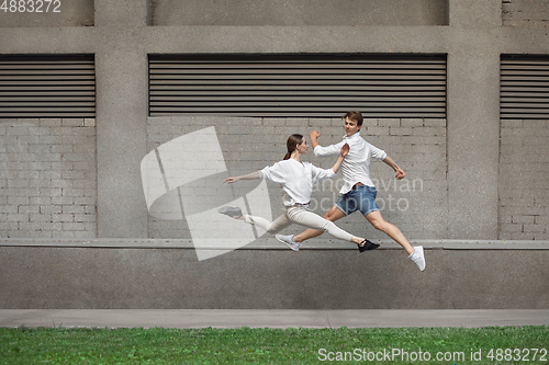 Image of Jumping young couple in front of buildings, on the run in jump high