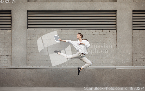 Image of Jumping young woman in front of buildings, on the run in jump high