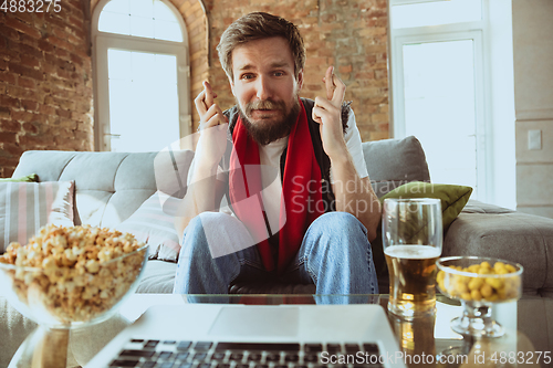 Image of Excited football fan watching sport match at home, remote support of favourite team during coronavirus pandemic outbreak