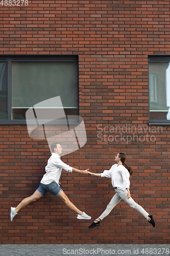 Image of Jumping young couple in front of buildings, on the run in jump high