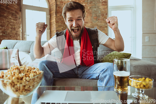 Image of Excited football fan watching sport match at home, remote support of favourite team during coronavirus pandemic outbreak