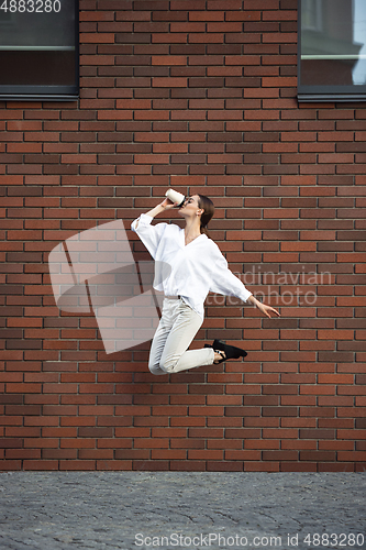 Image of Jumping young woman in front of buildings, on the run in jump high