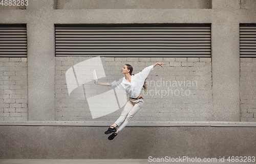 Image of Jumping young woman in front of buildings, on the run in jump high