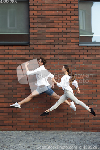 Image of Jumping young couple in front of buildings, on the run in jump high