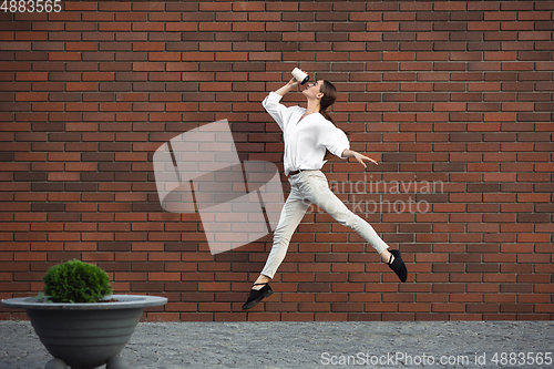 Image of Jumping young woman in front of buildings, on the run in jump high