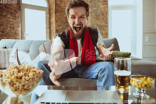 Image of Excited football fan watching sport match at home, remote support of favourite team during coronavirus pandemic outbreak