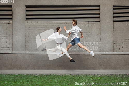 Image of Jumping young couple in front of buildings, on the run in jump high