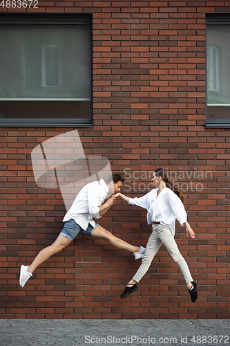 Image of Jumping young couple in front of buildings, on the run in jump high